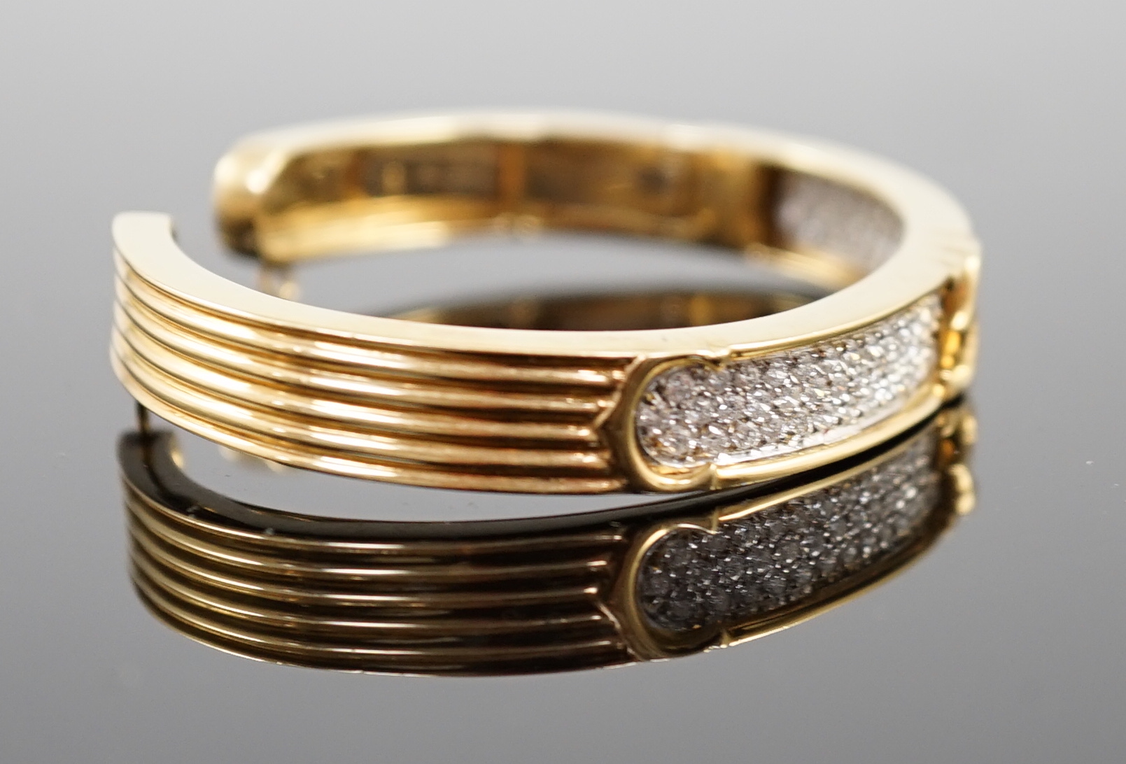 A modern 18k gold and pave set diamond Cartier open work hinged bangle